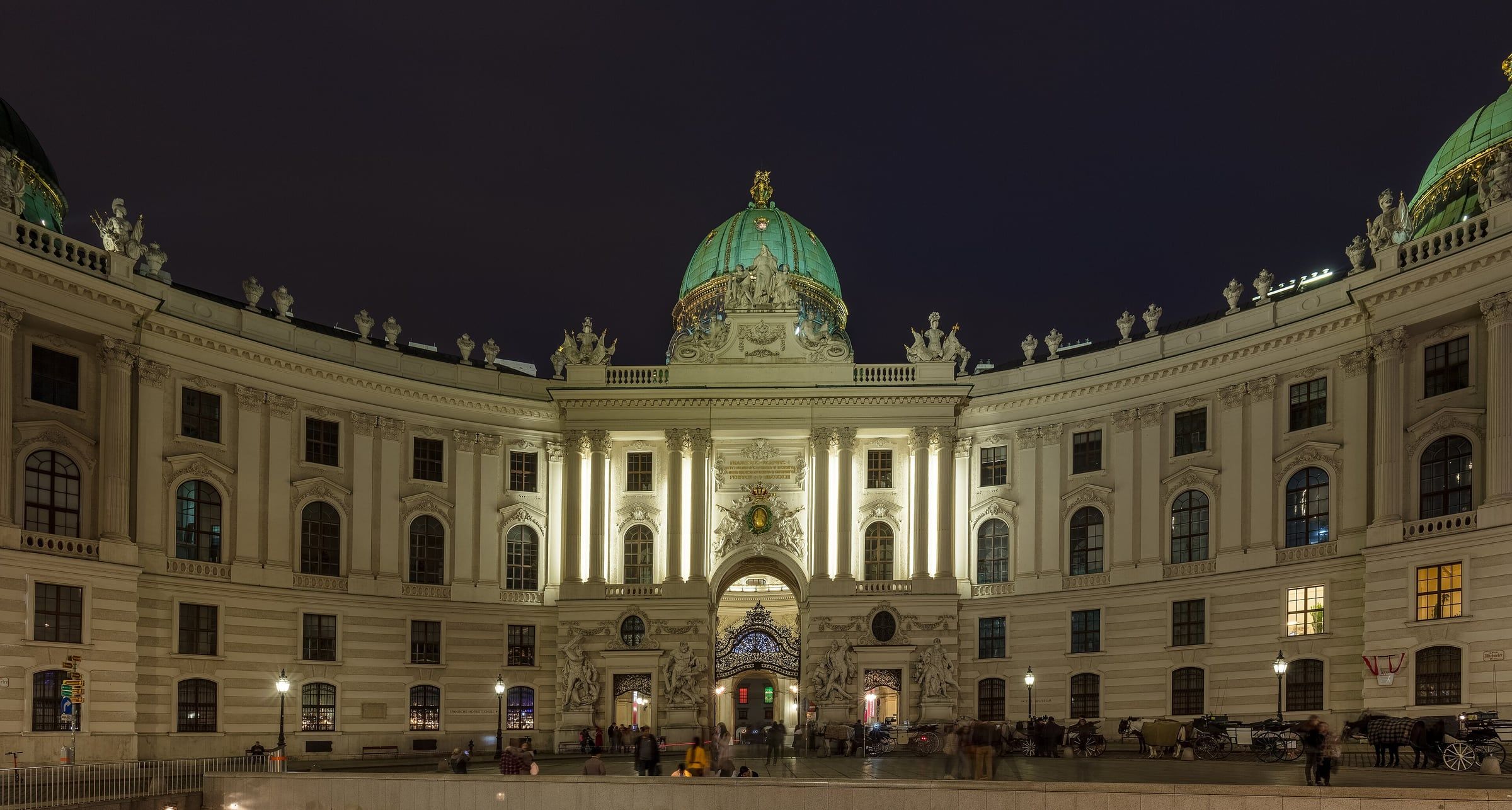 The domed Michaelertrakt entrance wing of the Hofburg Palace floodlit at night, with its curved wings framing the central facade.