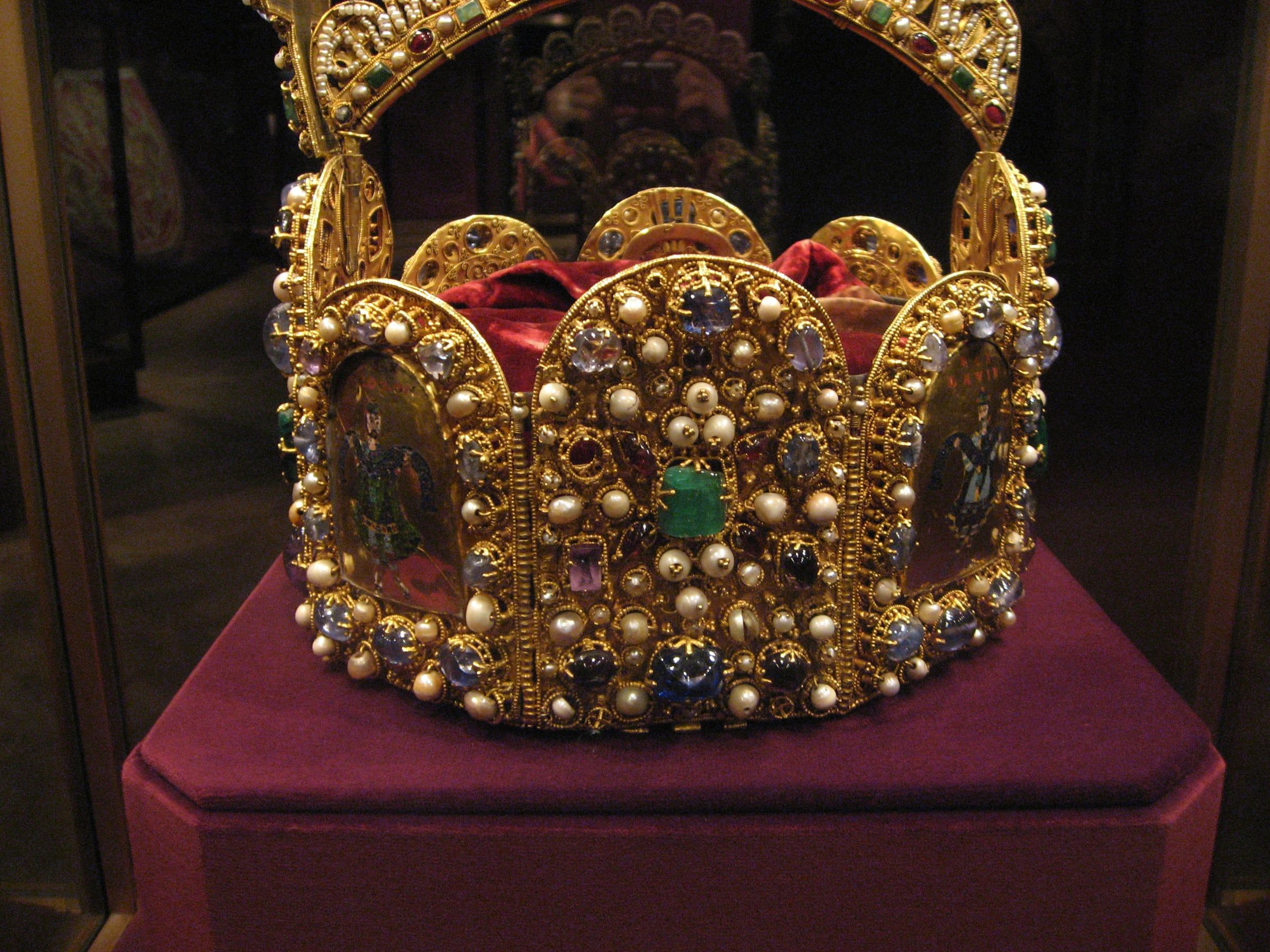 The jewelled Imperial Crown of the Holy Roman Empire in its glass case, with gold enamel panels and pearls on a crimson velvet base.